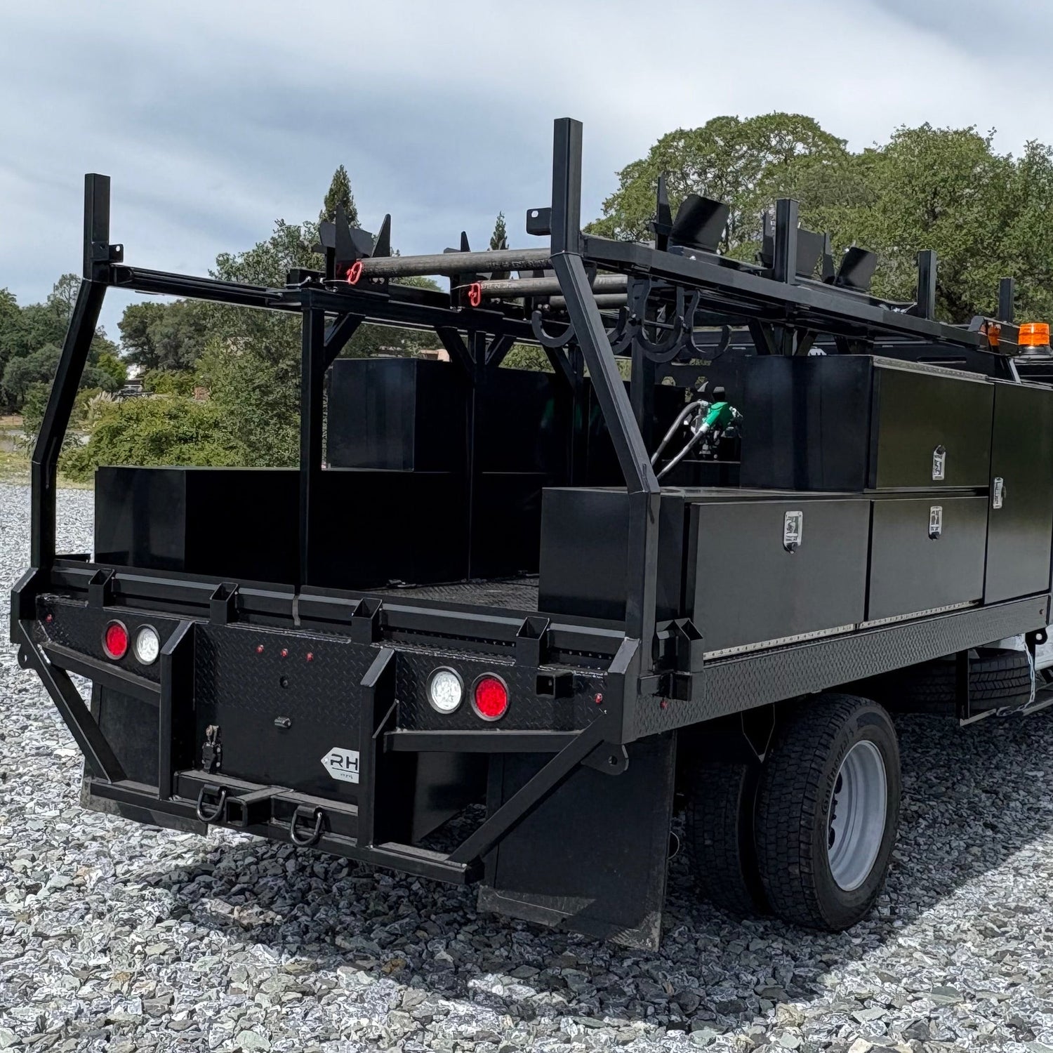 Black utility truck with equipment on a gravel surface with trees in the background