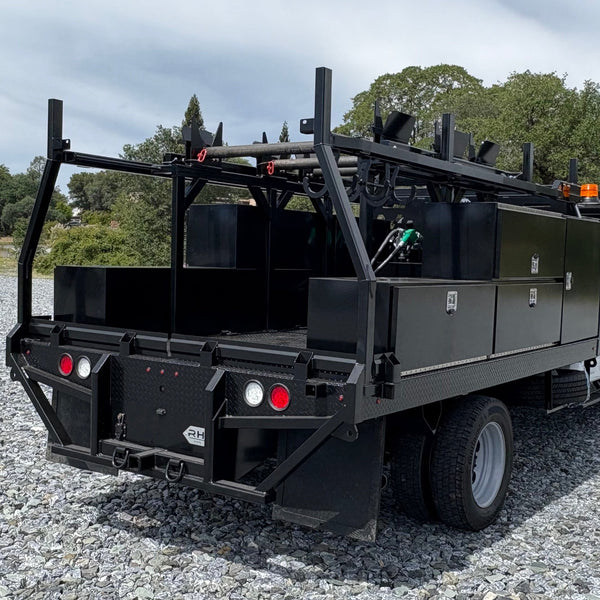 Black utility truck with equipment on a gravel surface with trees in the background