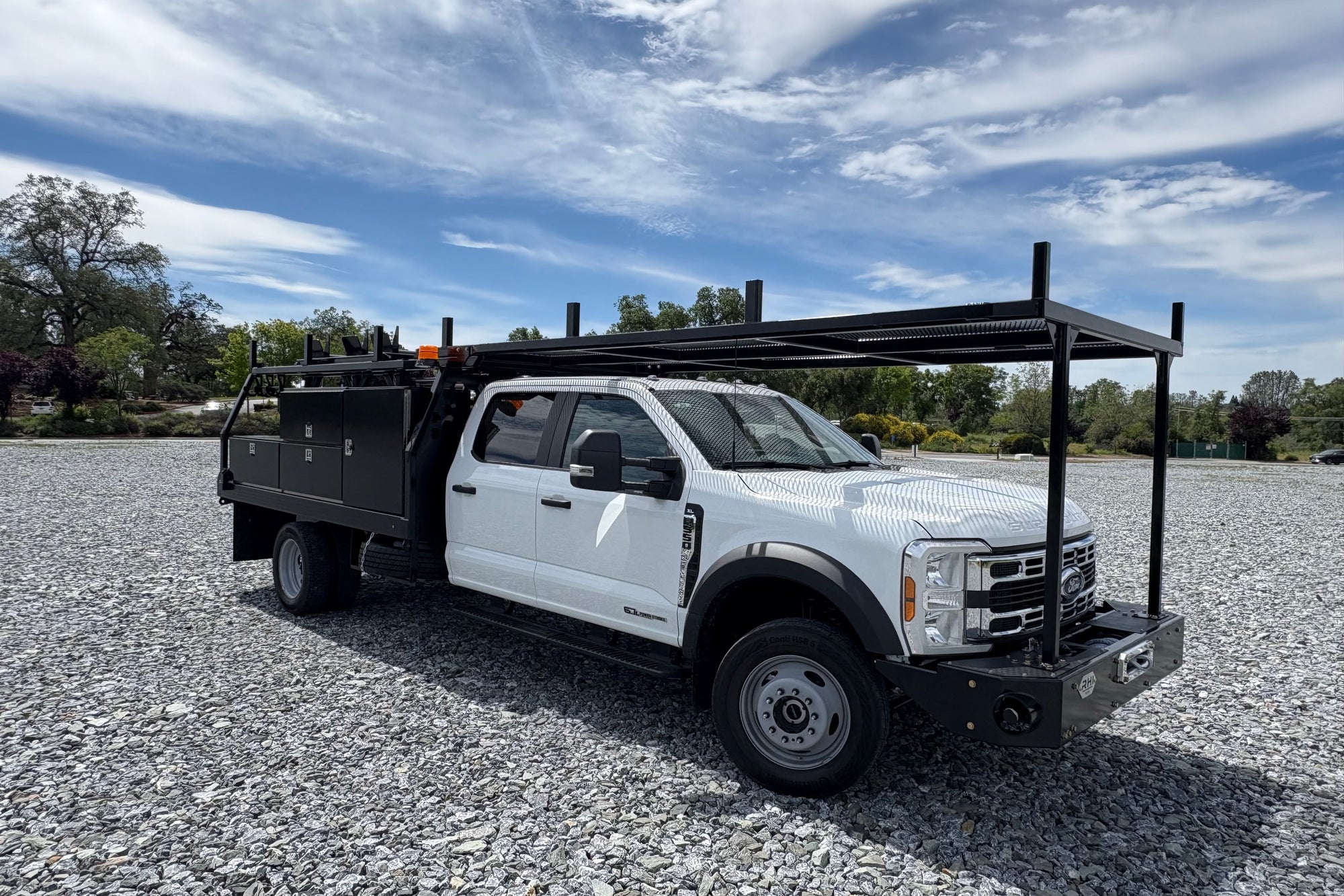 White pickup truck with a large toolbox on a gravel surface under a blue sky.