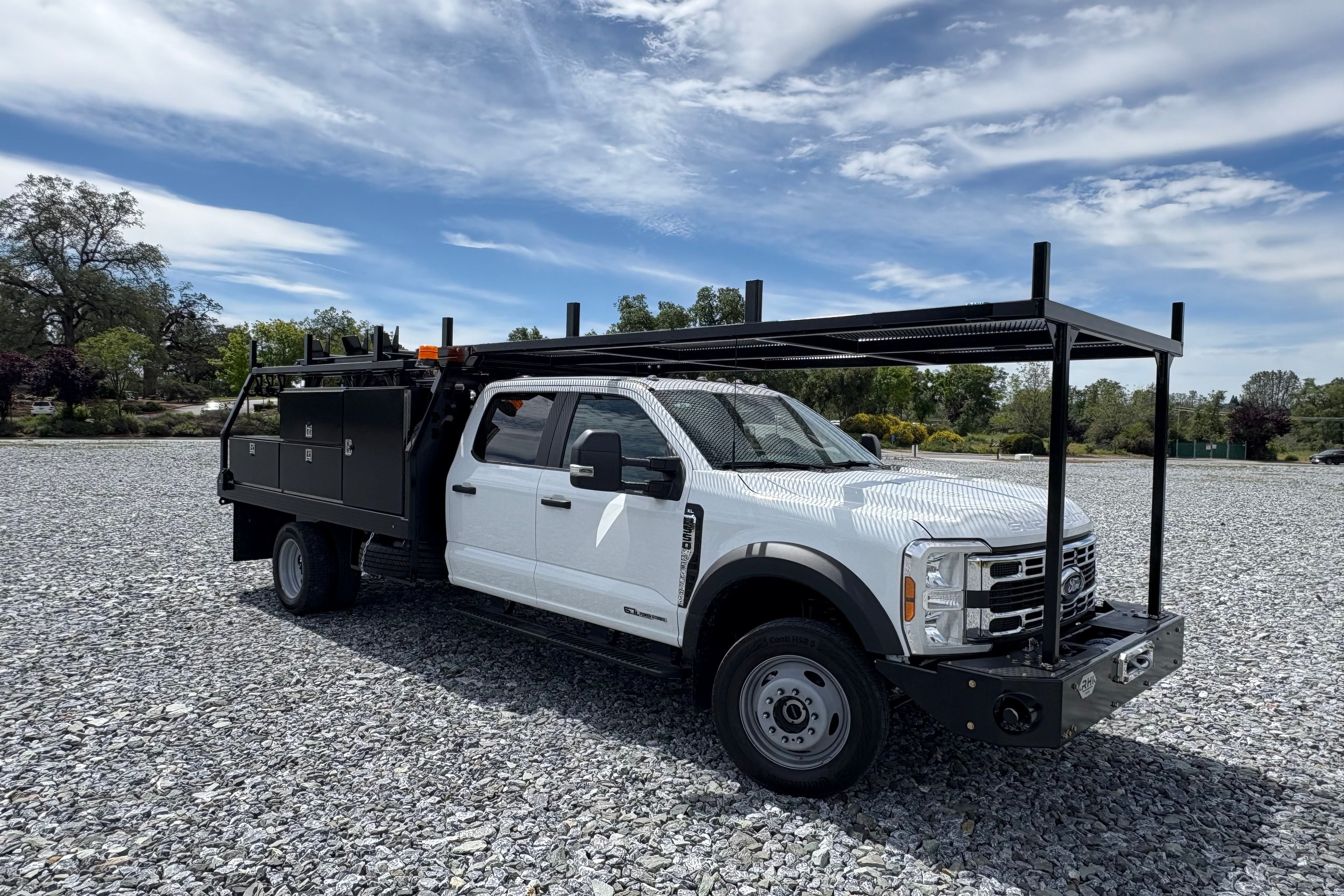 White pickup truck with a large toolbox on a gravel surface under a blue sky.